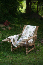 Palm Plume European linen palm throw styled on an outdoor chair in a garden setting.