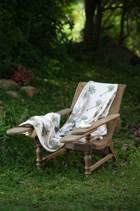 Palm Plume European linen palm throw styled on an outdoor chair in a garden setting.