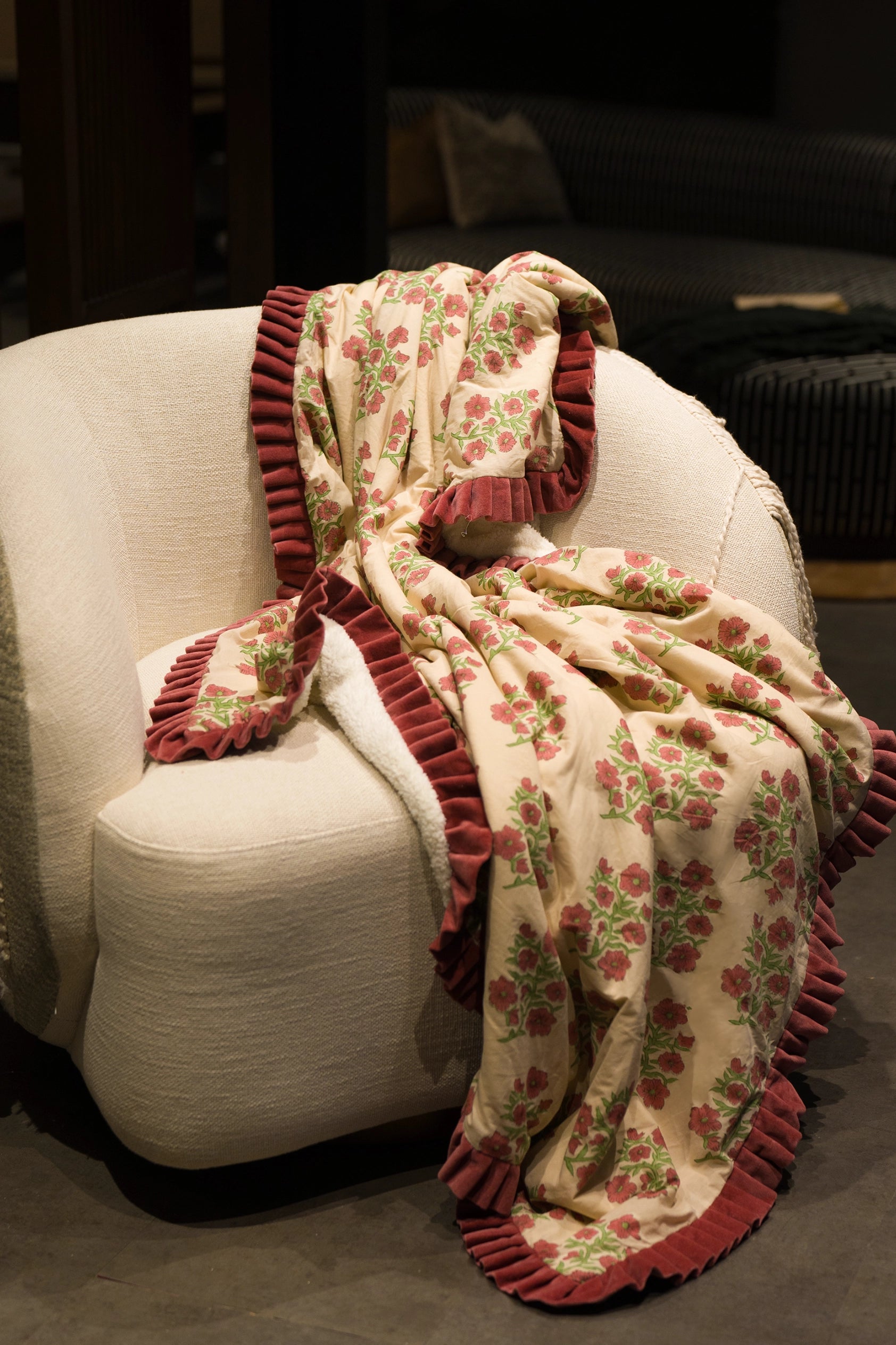 Pink floral hand block print sherpa throw blanket with red velvet styled on an armchair in a living room.