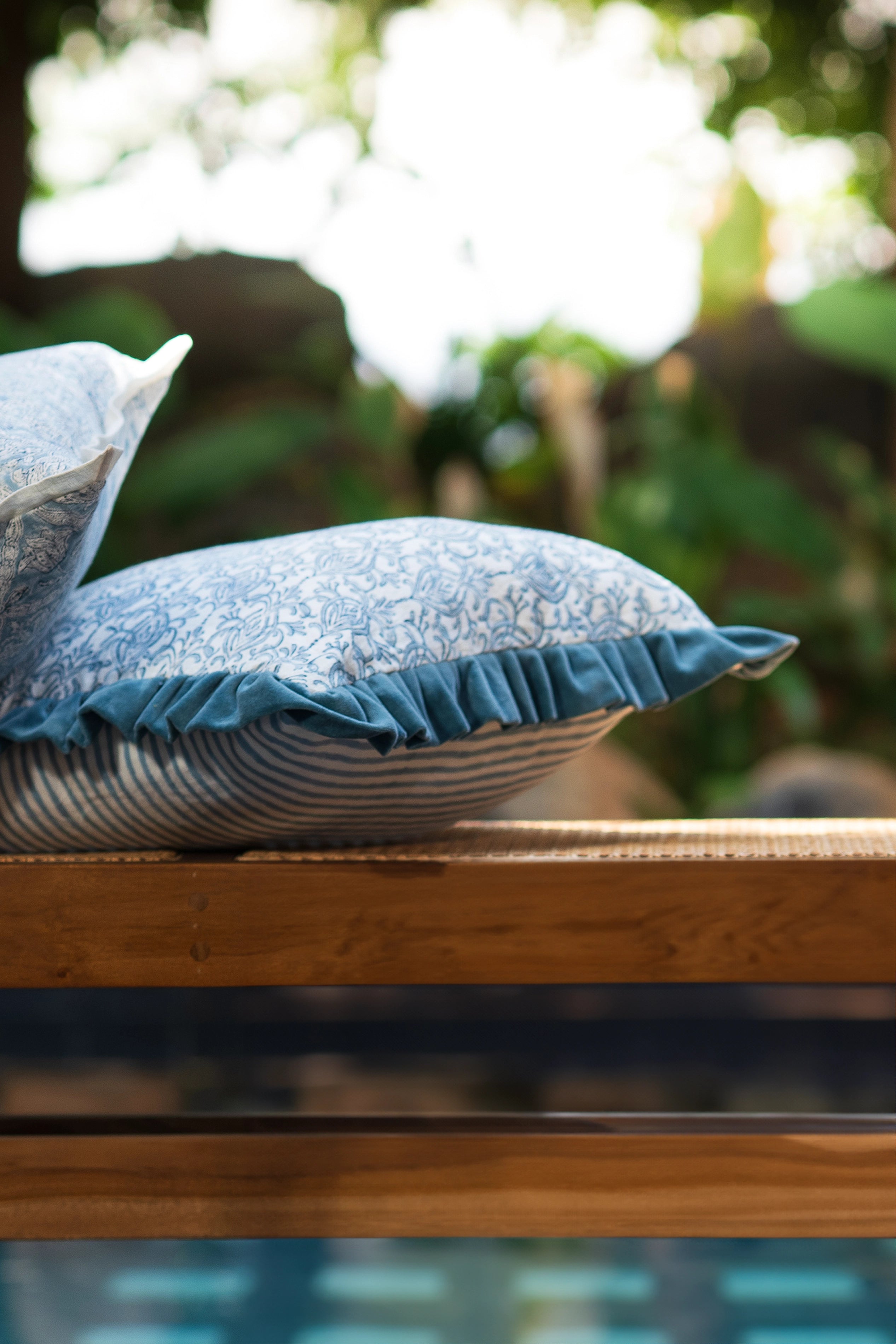 Blue hand block print European flax linen cushion with teal velvet ruffle styled outdoors.