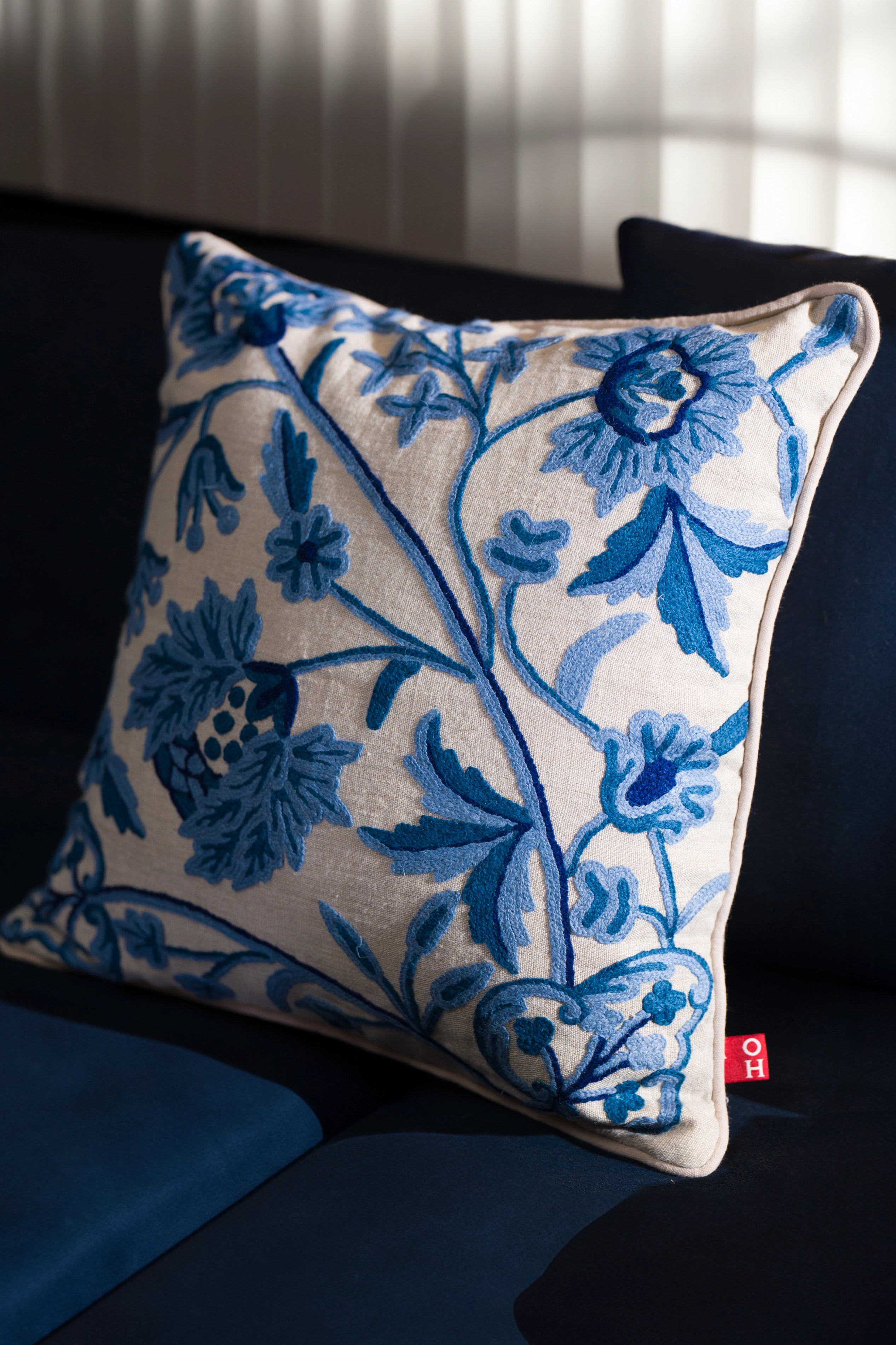 Blue crewel embroidered linen cushion styled on outdoor seating.