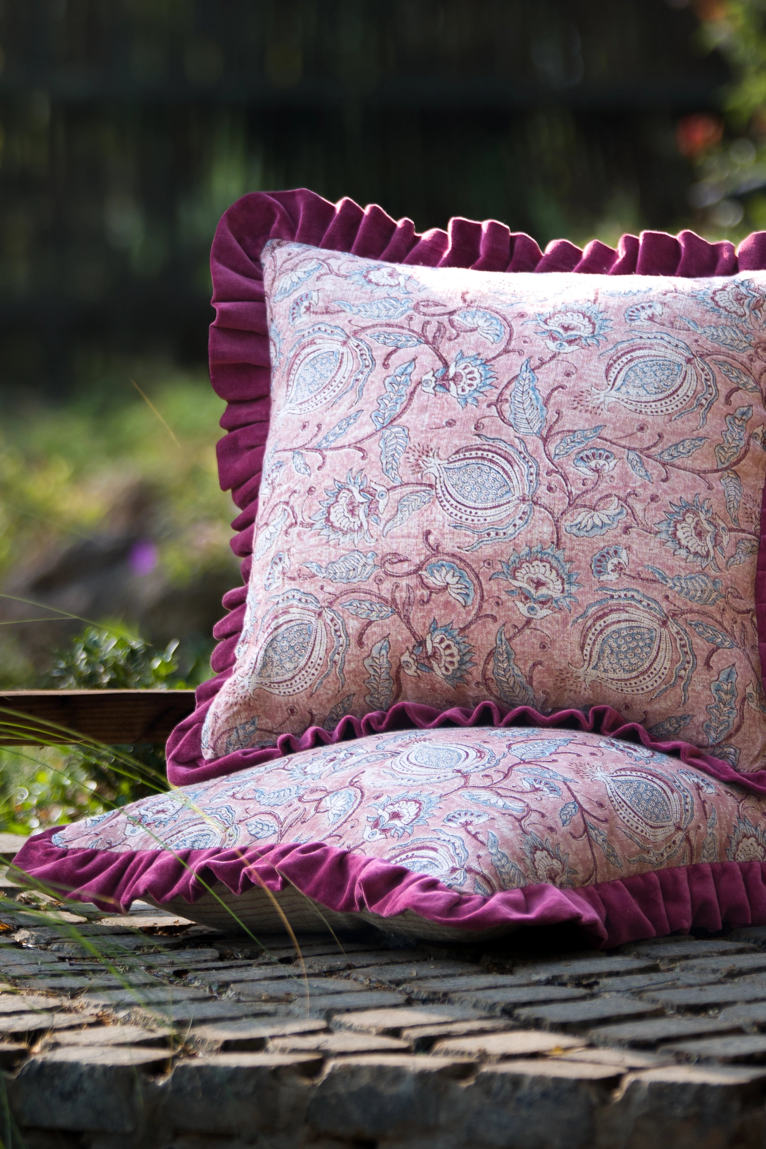 Square pink floral hand block print linen cushion with ruffled edge styled outdoors.