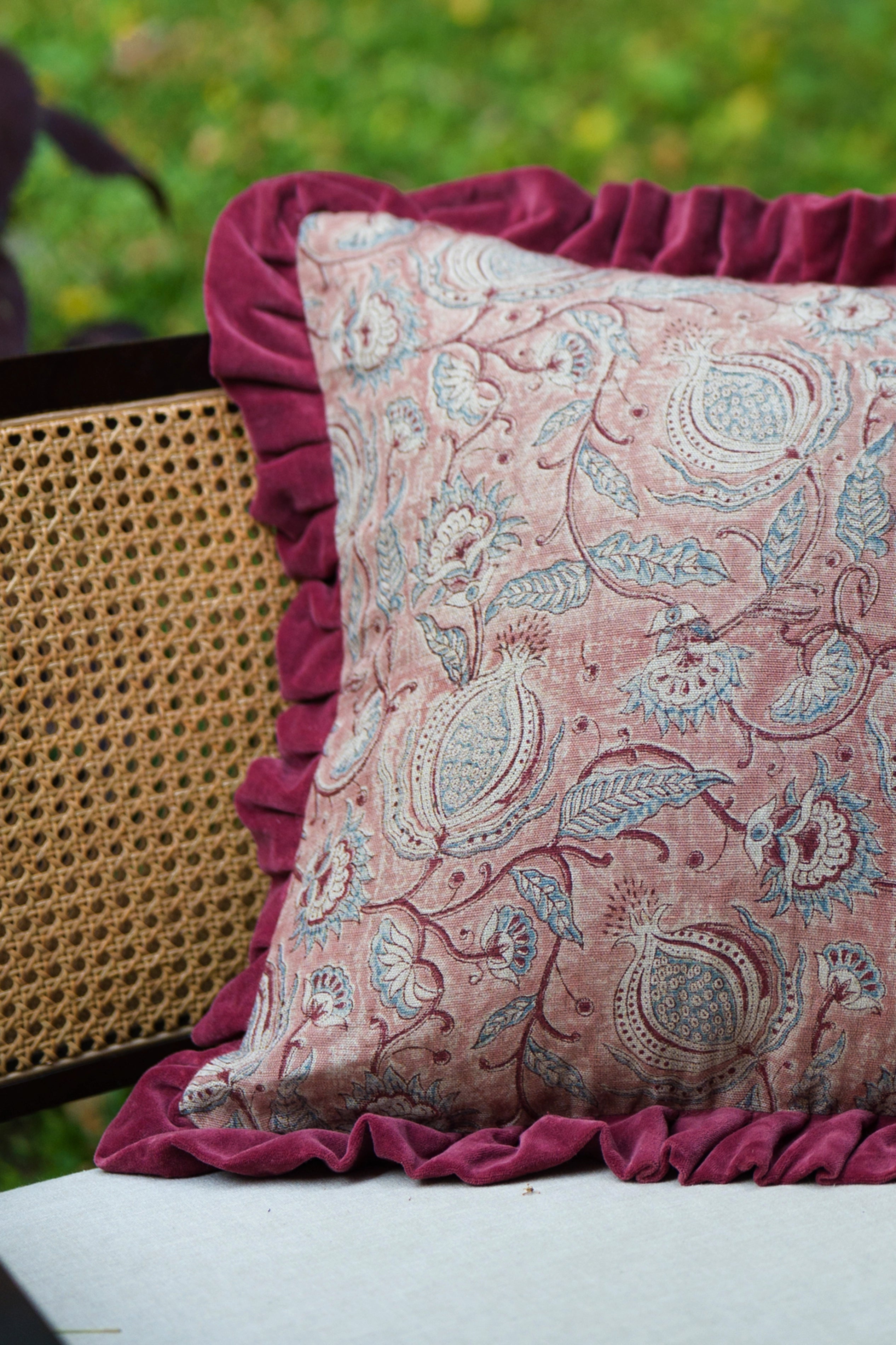 Square pink floral hand block print linen cushion with ruffled edge styled on outdoor seating.