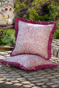 Square pink floral hand block print paisley pattern linen cushion with ruffled edge styled on a chair outdoors.