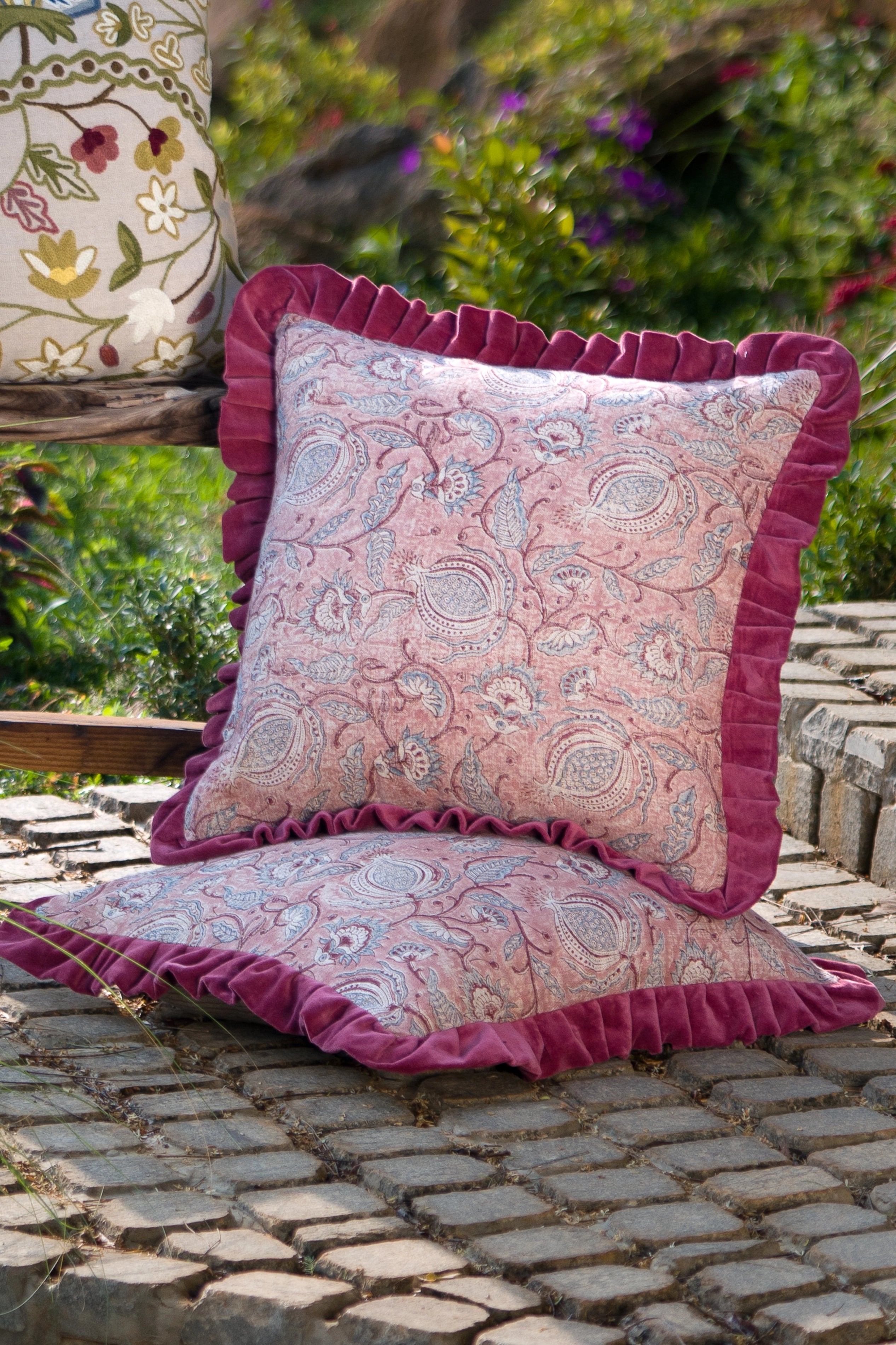 Square pink floral hand block print paisley pattern linen cushion with ruffled edge styled on a chair outdoors.