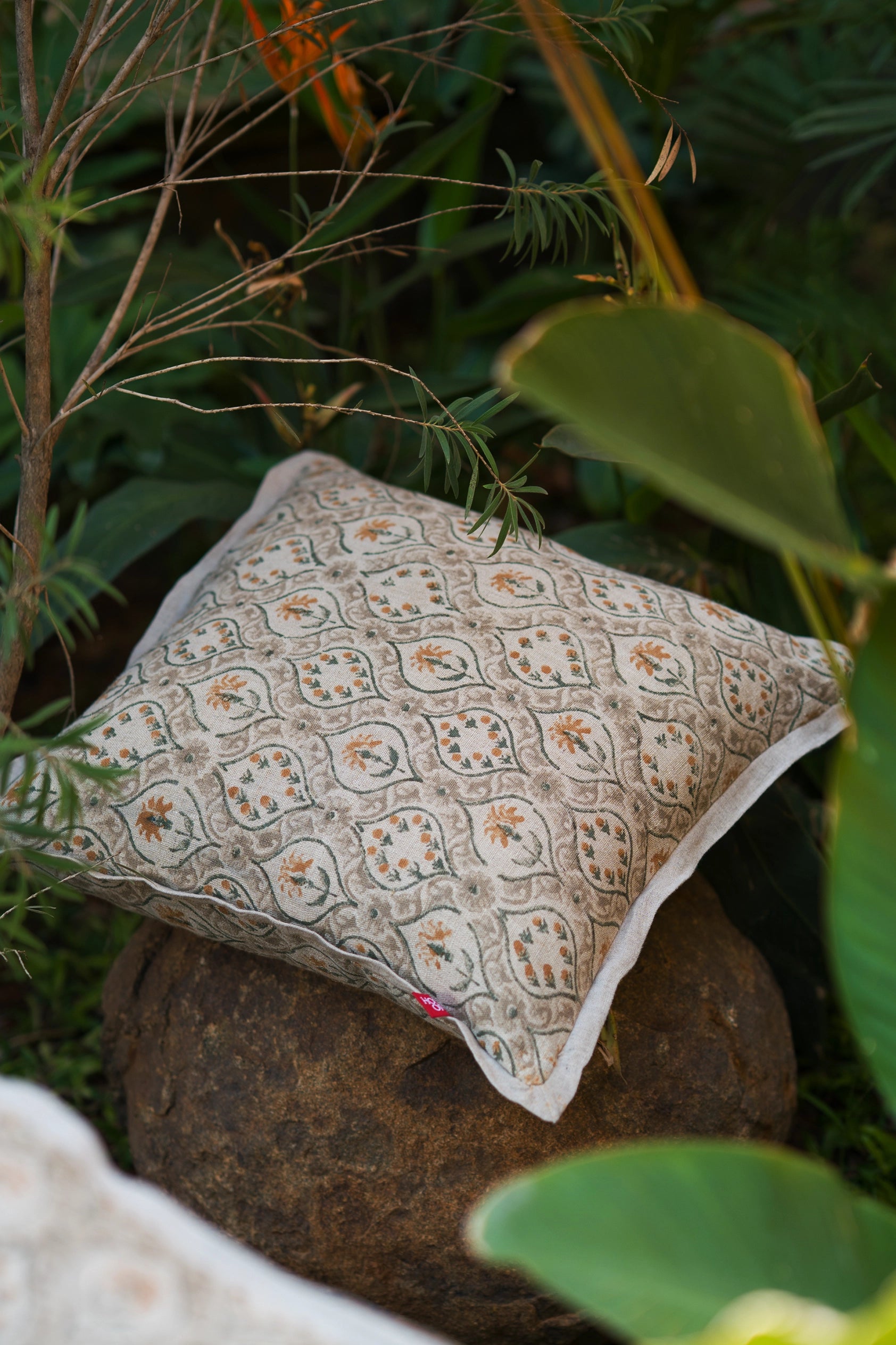 Taupe hand block print European flax linen cushion styled outdoors among green foliage.