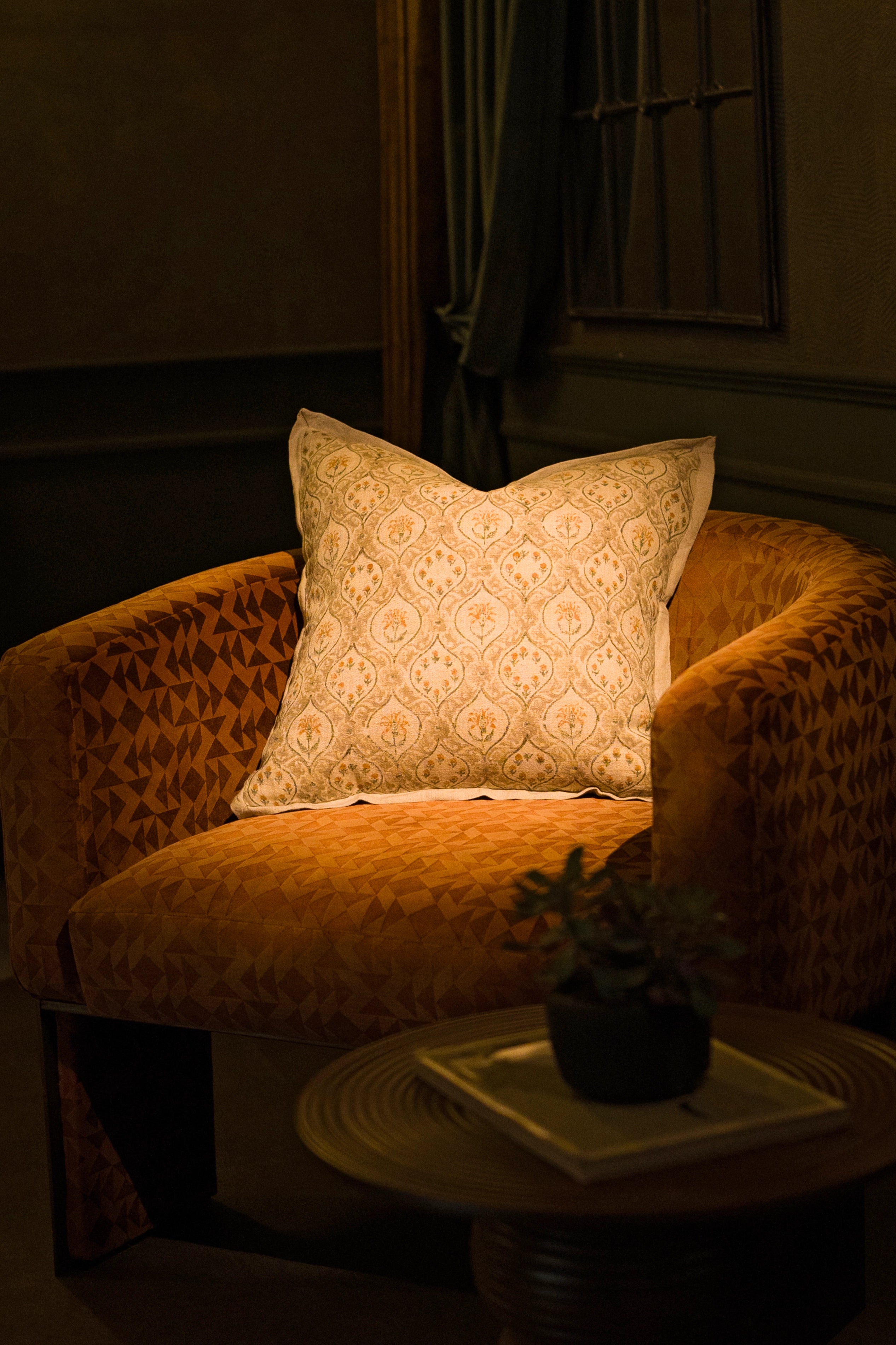 Taupe hand block print European flax linen cushion styled on an armchair beside a table lamp.