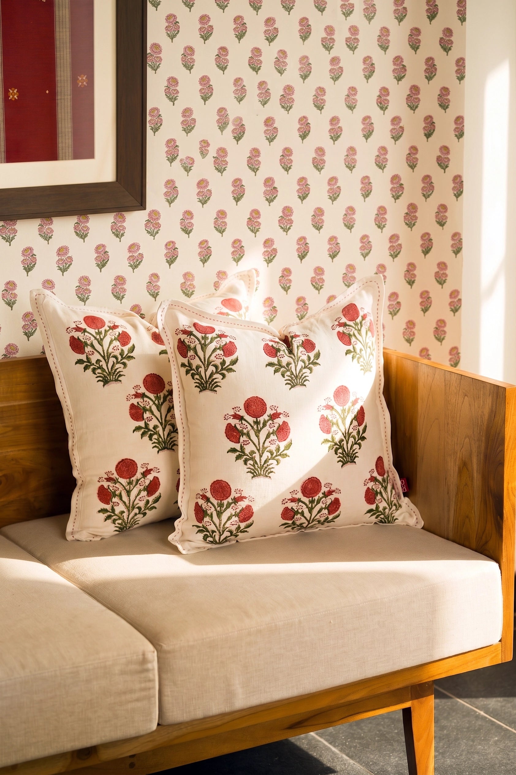 Square pink floral hand block print linen cushion styled on a sofa with coordinating cushions.
