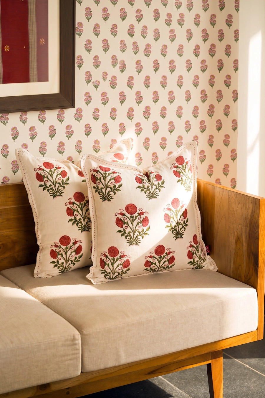 Square pink floral hand block print linen cushion styled on a sofa with coordinating cushions.