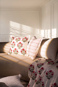 Square pink floral hand block print linen cushion styled on a sofa in a sunlit living room.