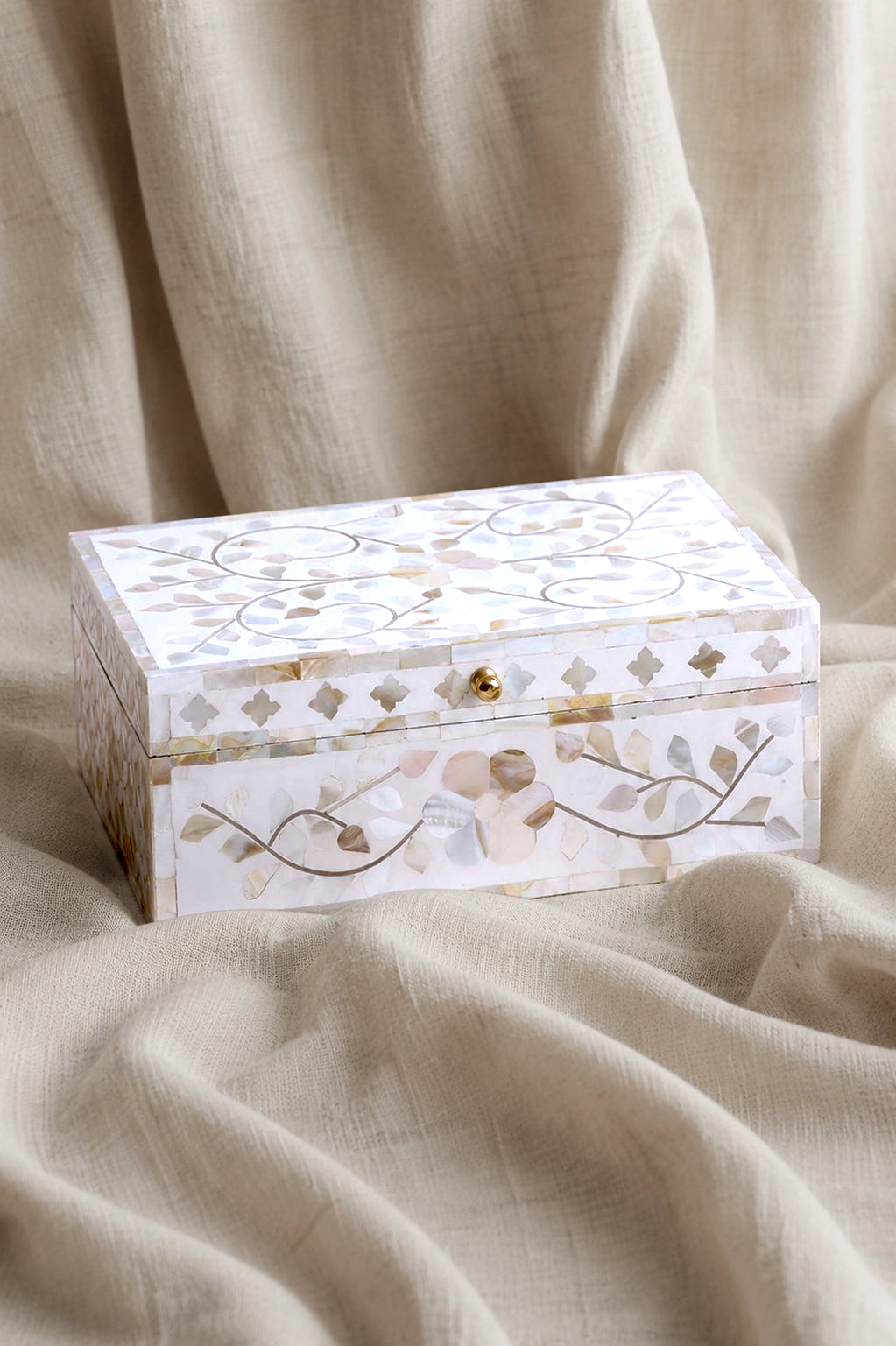 House of H Clover Box with iridescent Mother of Pearl floral inlay and a small brass knob on a draped linen fabric.